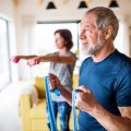 Older man and woman exercising at home with elastics and weights.